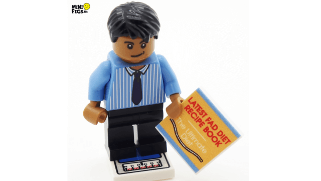 A Lego figure holds a book entitled "LATEST FAD DIET RECIPE BOOK", illustrating the reality that resolutions rarely work